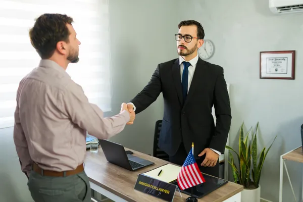 An immigration attorney shaking hands with a client across a desk in a law office