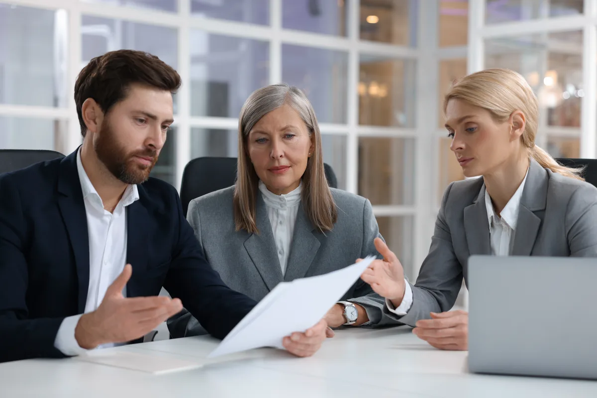 An independent insurance agent reviewing coverage options with two clients across a desk in a bright office