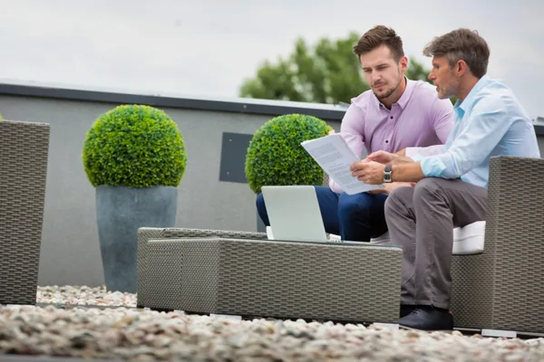 A landscaping company owner reviewing marketing performance on a laptop with a consultant beside a finished paver patio job