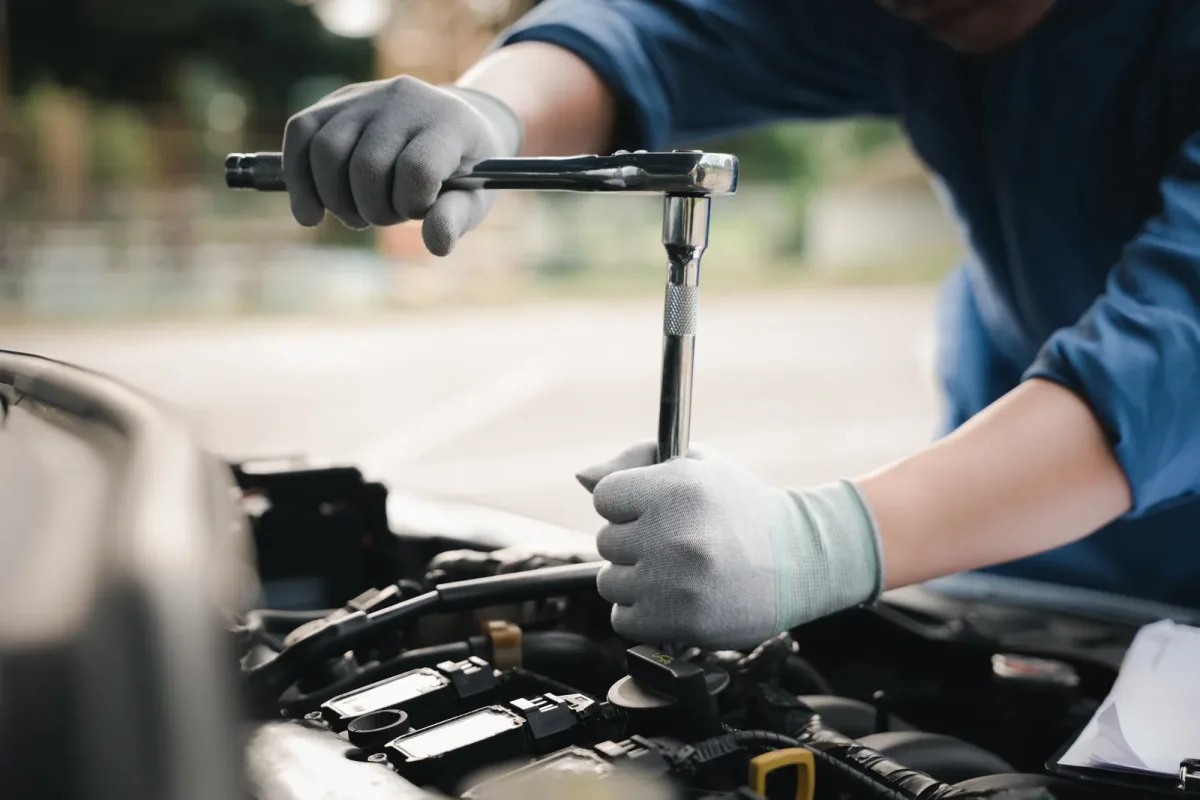 Mobile mechanic working under the open hood of a car in a customer's driveway beside his service van