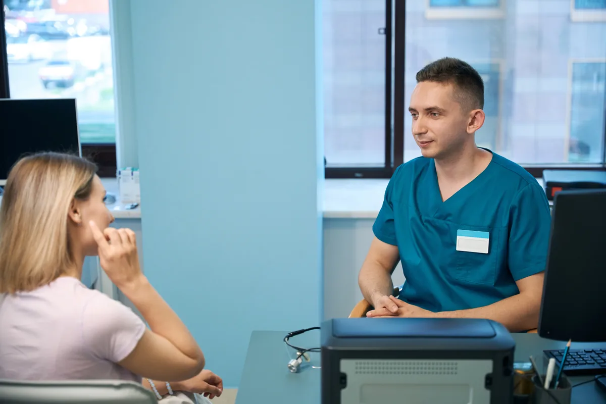 An oral and maxillofacial surgeon discussing a treatment plan with a seated patient in a bright clinic consultation room