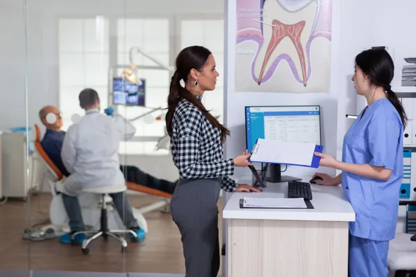 Orthodontist and practice manager reviewing new-patient consultation numbers at a clinic front desk