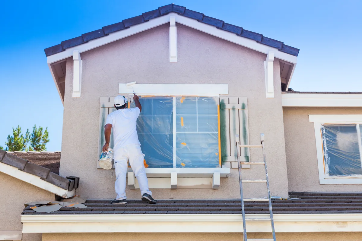 A professional painter on a ladder applying fresh paint to the exterior trim of a residential home