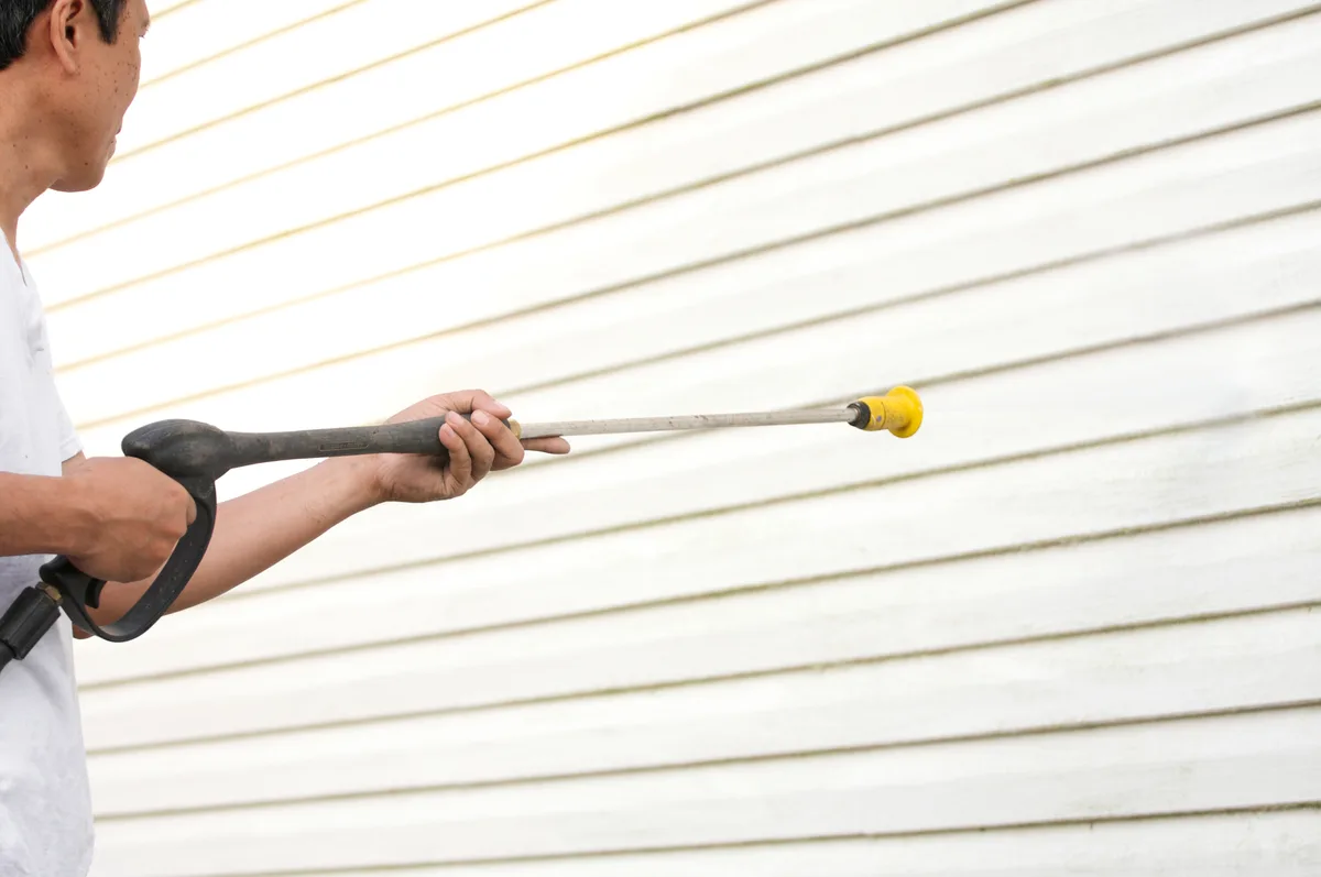 Pressure washing technician cleaning the exterior of a house with a spray wand on a sunny day