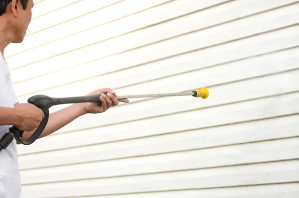 Pressure washing technician cleaning the exterior of a house with a spray wand on a sunny day