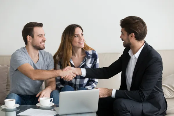 A property manager shaking hands with a rental property owner across a desk in a bright office