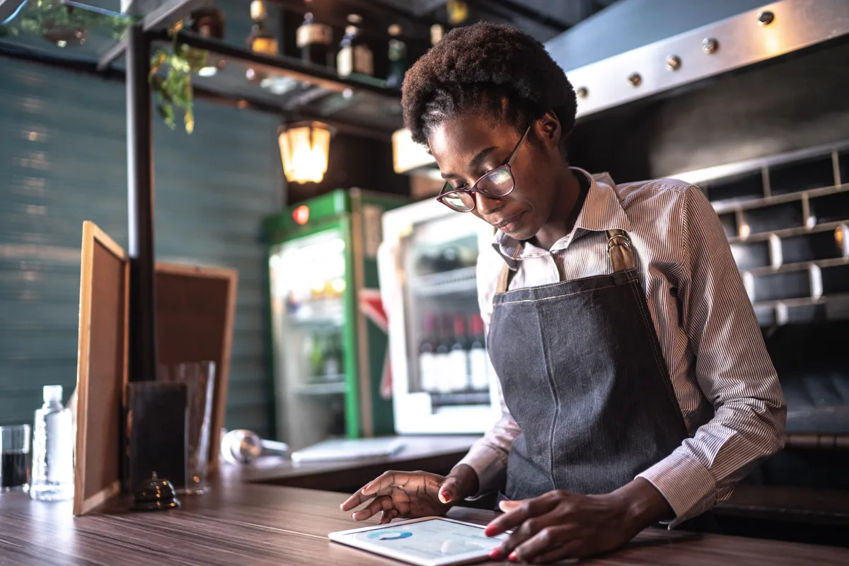Restaurant owner reviewing reservation and marketing data on a tablet at the host stand