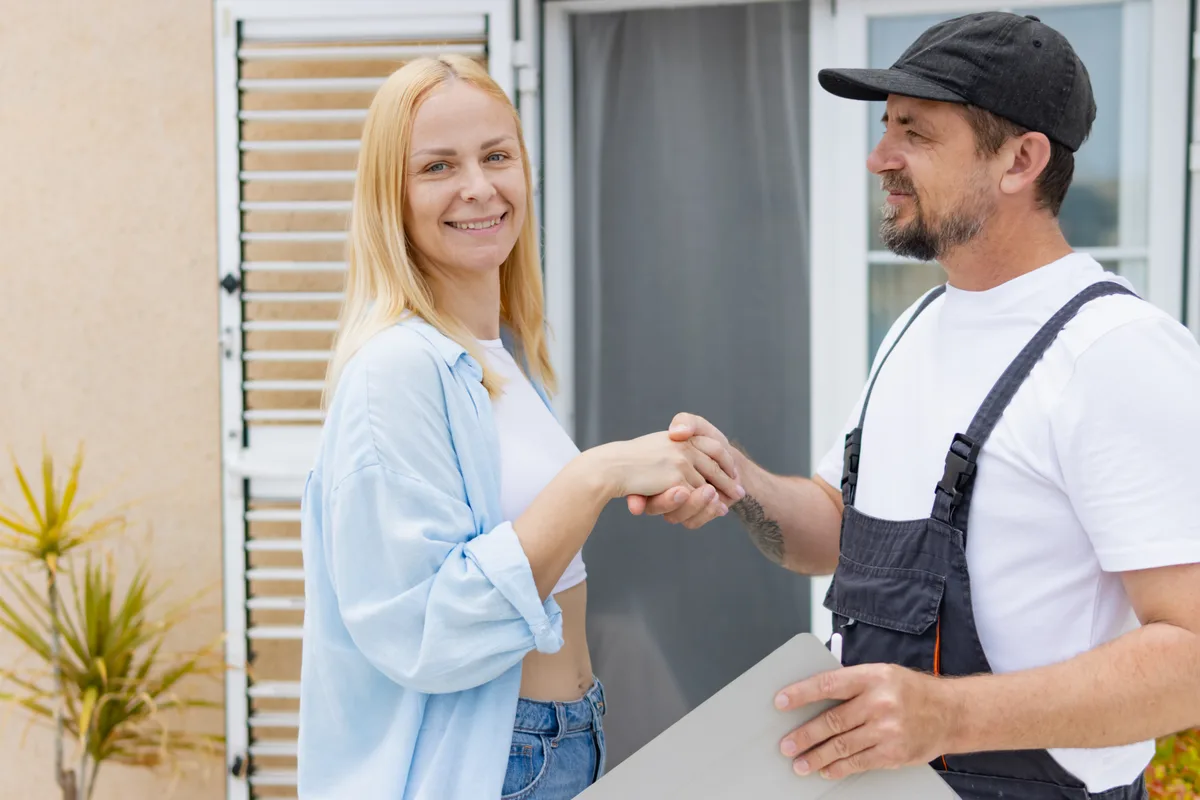 A roofing company owner meeting with a homeowner in front of a house with a newly installed shingle roof