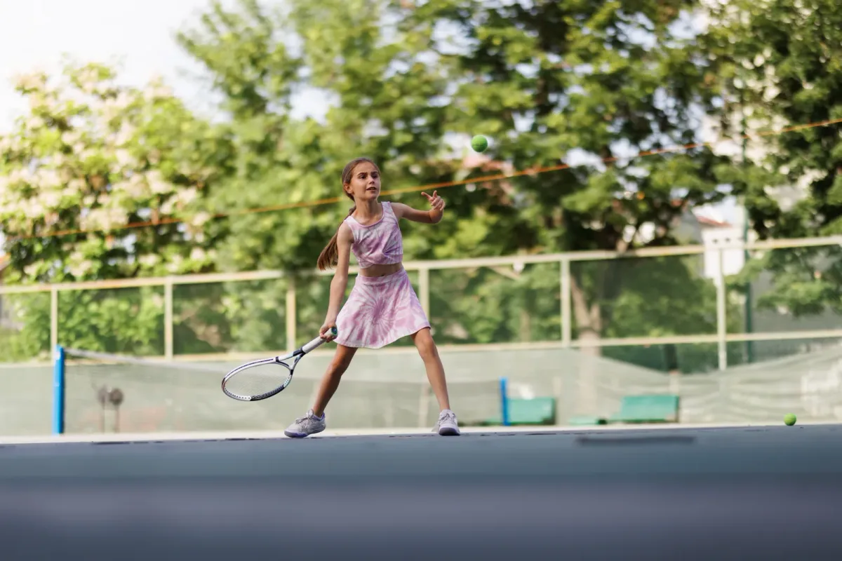 A tennis coach demonstrating a serve to a junior player on an outdoor academy court