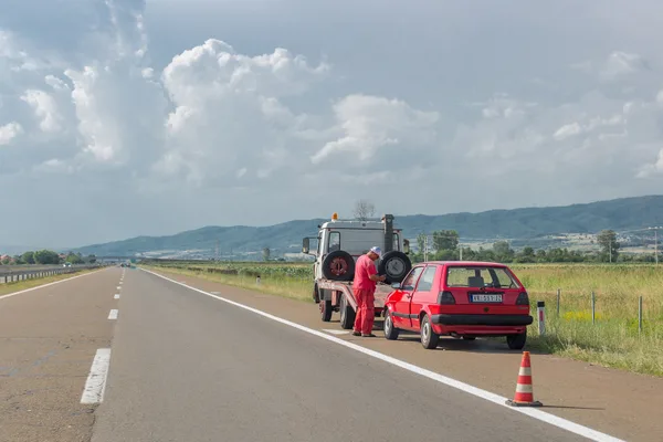 A tow truck operator winching a disabled car onto a flatbed at the side of a road