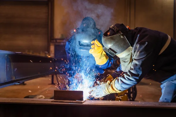 An instructor coaching an adult student at a welding station inside a trade school workshop