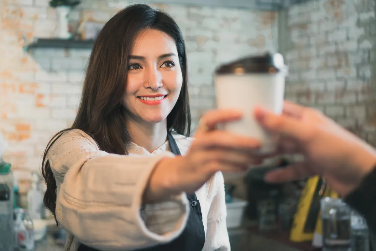 Barista handing a takeaway coffee to a customer across a busy café counter