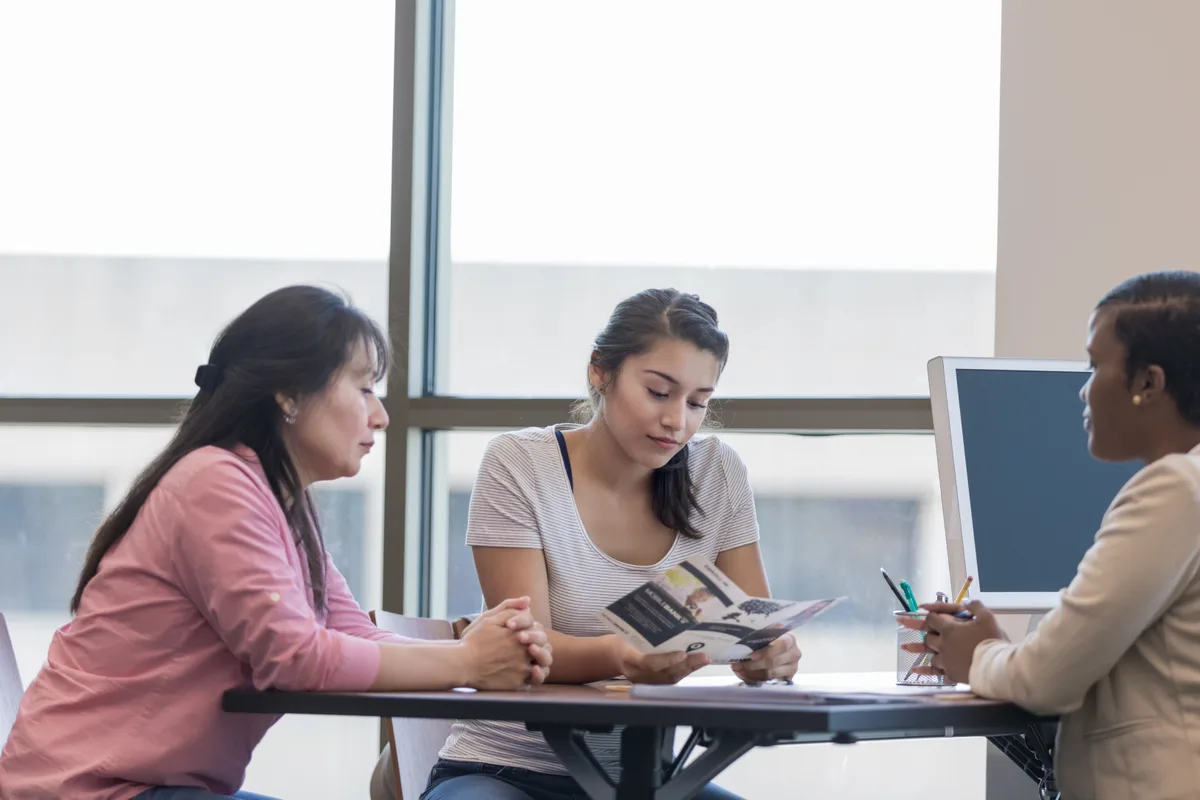 An admissions consultant reviewing a college application plan with a high school student and parent across a desk