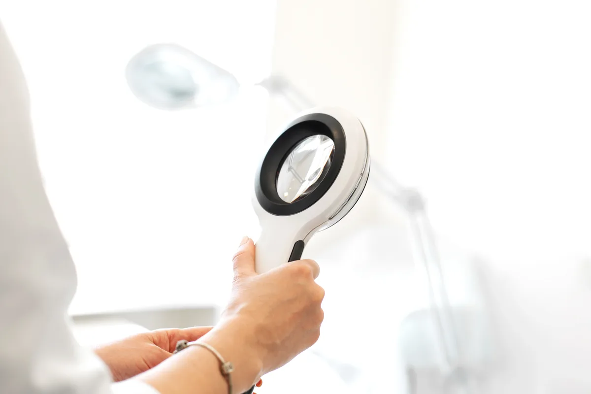 Board-certified dermatologist examining a patient's skin with a dermatoscope during a clinic consultation