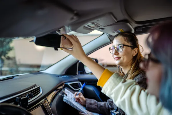 A certified driving instructor coaching a teenage learner from the passenger seat during a behind-the-wheel lesson