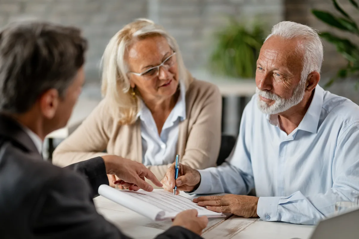 Estate planning attorney reviewing trust documents across a desk with an older married couple in a law office