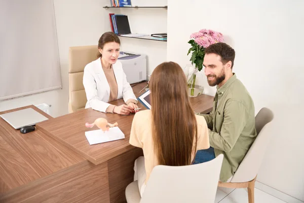 A reproductive endocrinologist explaining treatment options to a hopeful couple during a fertility clinic consultation