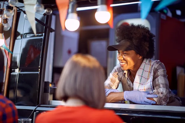 Food truck operator handing an order to a customer at the service window during a busy lunch shift