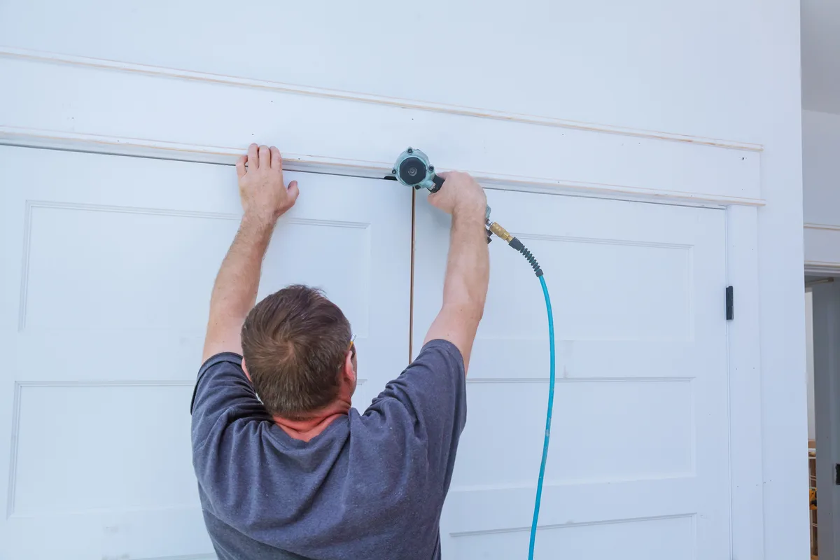 Garage door technician servicing a residential overhead door in a suburban driveway