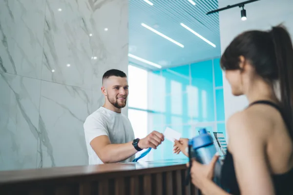 A studio owner greeting a new member at the front desk of a modern gym