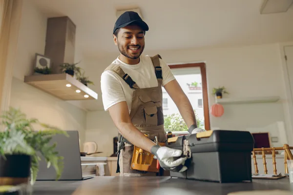 A handyman in a homeowner's kitchen using a drill to mount a cabinet, tool bag open beside him