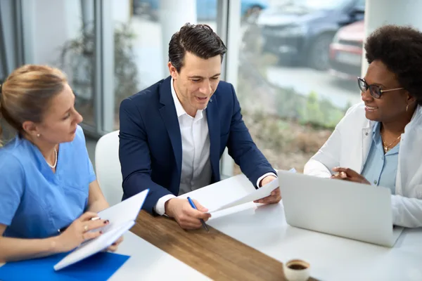 An independent insurance agent reviewing auto and home coverage options with a couple across a desk in an agency office