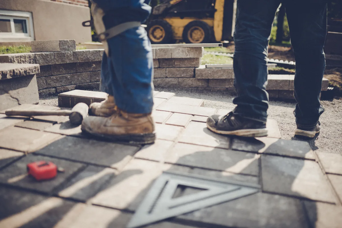 Landscaping crew installing a paver patio in a residential backyard on a sunny day