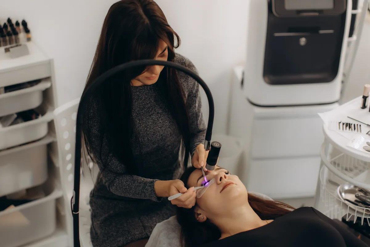 Lash artist applying volume eyelash extensions to a reclining client in a bright modern lash and brow studio