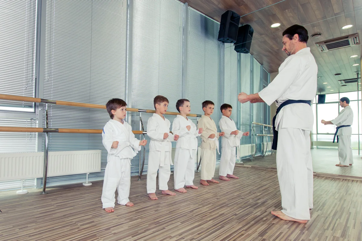 A martial arts instructor leading a line of children through a karate drill in a bright, modern dojo