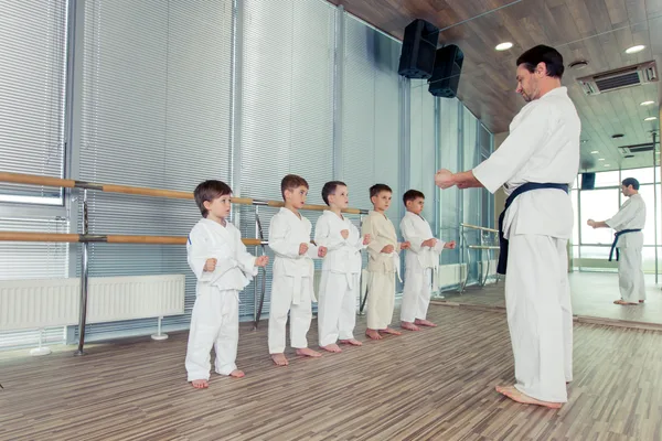 A martial arts instructor leading a line of children through a karate drill in a bright, modern dojo