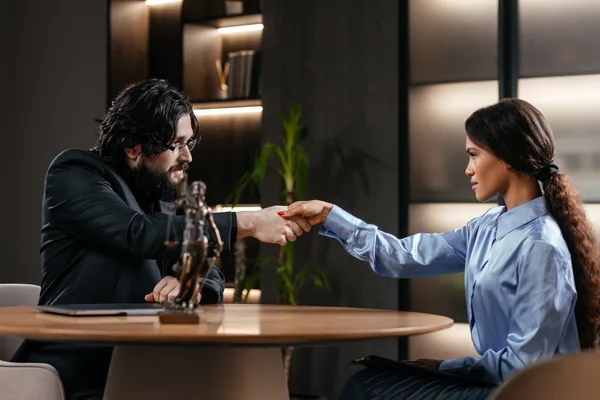 A personal injury attorney shaking hands with a client across a desk in a bright law office