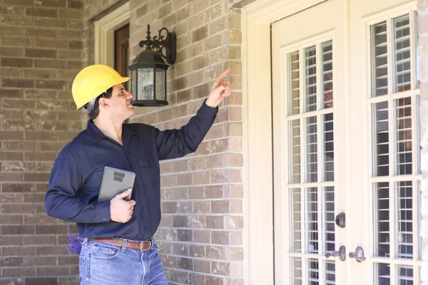 Pest control technician inspecting the foundation of a home while reviewing notes on a tablet