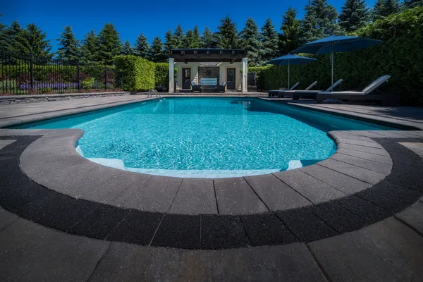 Newly built luxury inground swimming pool with stone patio and landscaping in a Canadian backyard