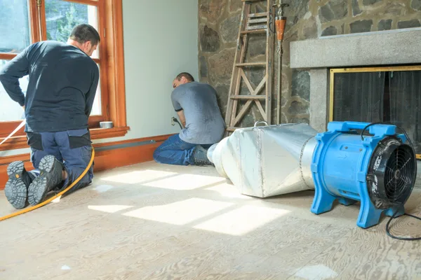 Restoration technician positioning air movers to dry a flooded room after water damage