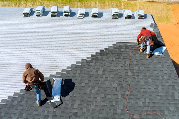 A professional roofing crew installing asphalt shingles on a steep residential roof on a clear day
