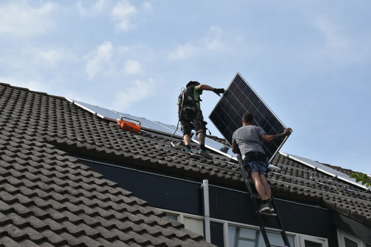 Two solar technicians installing photovoltaic panels on a residential roof on a clear day