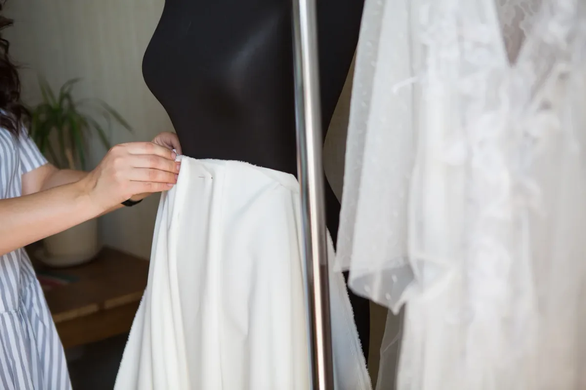 Tailor pinning the hem of a suit jacket during a fitting while the customer stands and waits