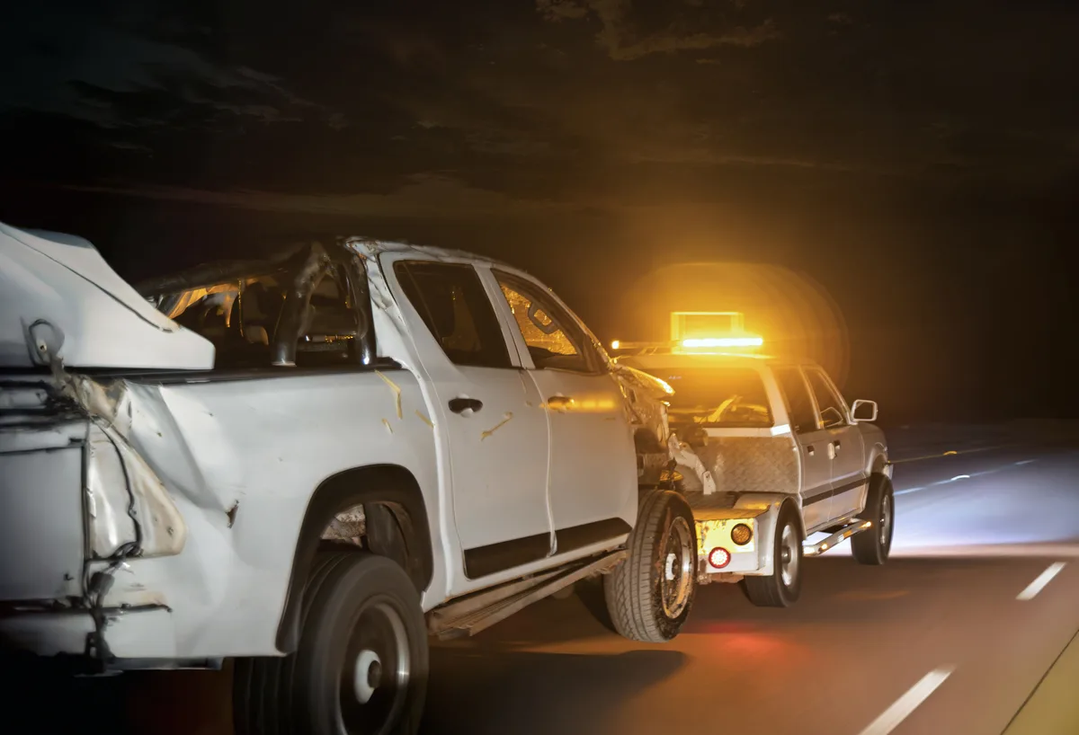Tow truck operator winching a car onto a flatbed at the roadside at night