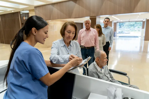 A patient checking in at an urgent care clinic front desk while staff assist at a computer