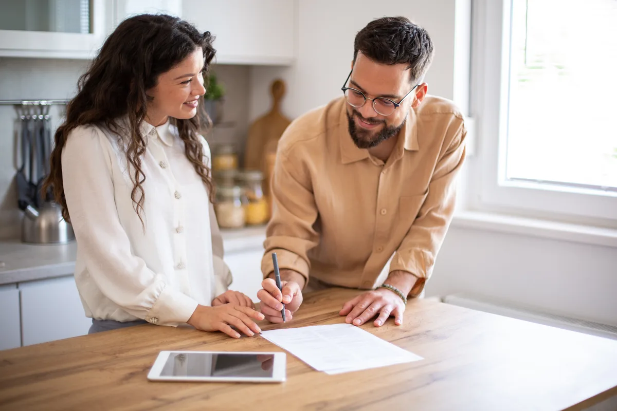 Real estate investor reviewing a cash-offer contract with a homeowner at a kitchen table