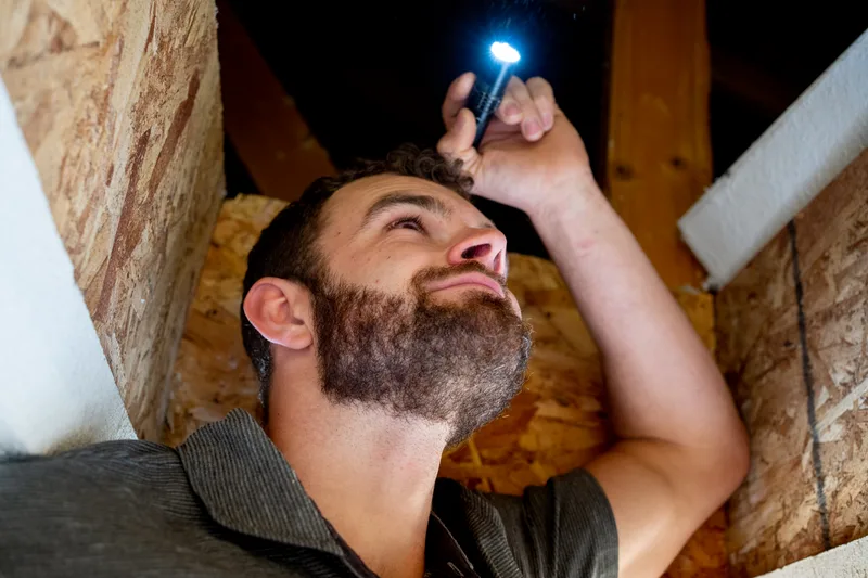 A Beacon repair lead shining a flashlight along the rafters in an attic, tracing where water gets in