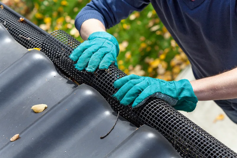 Gloved hands fitting a mesh leaf guard into a dark metal gutter