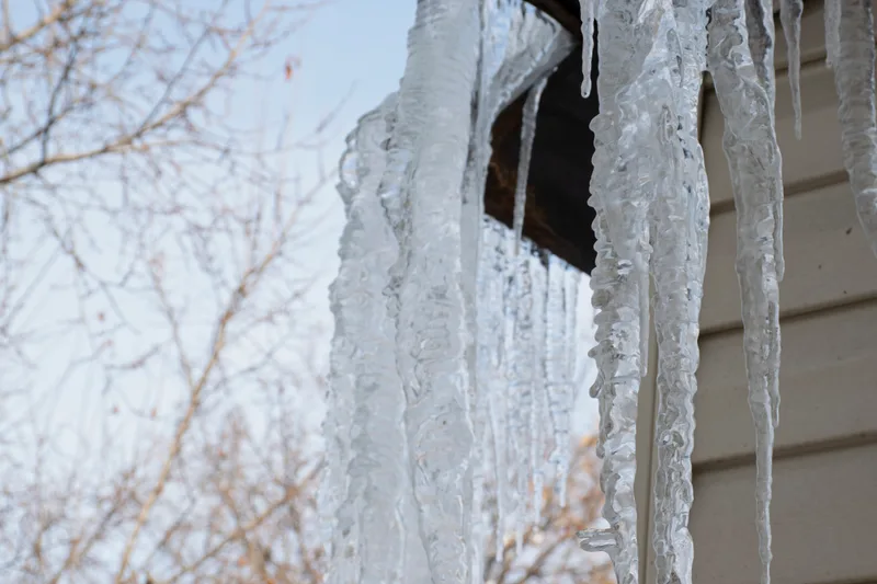 Long icicles hanging from a frozen roof edge, the sign of an ice dam forming above