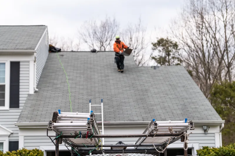 A Beacon job in progress: roof-edge staging and ladders along a grey shingle roof, a roofer working near the ridge