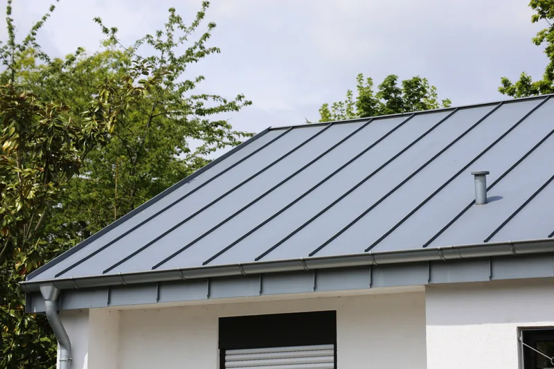 Grey standing-seam metal roof with crisp vertical panel lines over a white-walled house