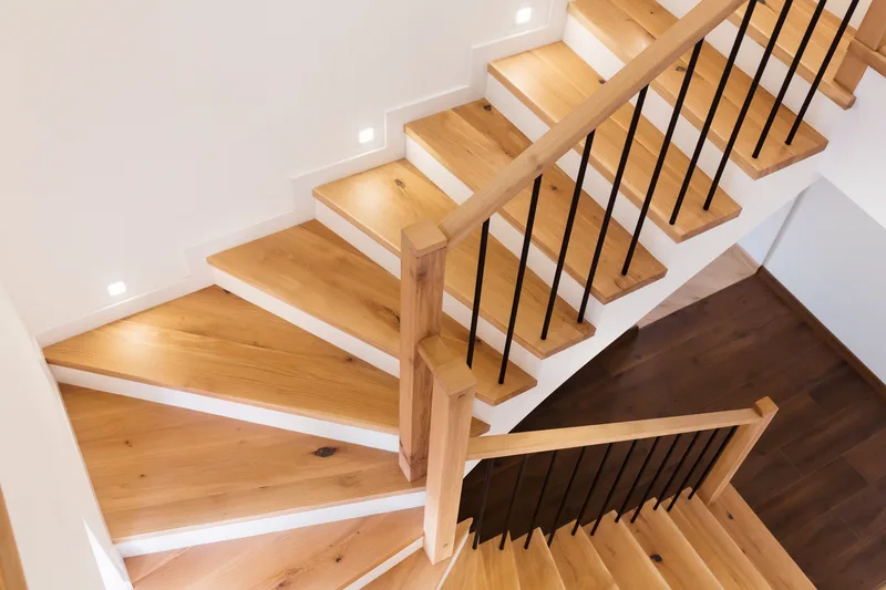 A white-oak stair with black steel balusters rising through a bright white stairwell
