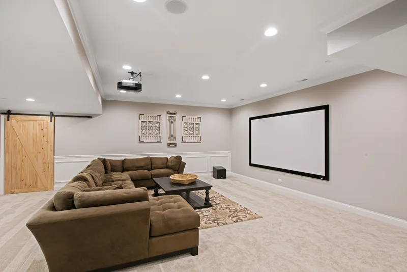 Finished basement media room with a sectional sofa, a large wall screen, and a barn door