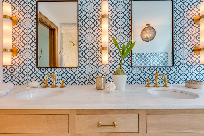 Remodeled bathroom with blue and white patterned tile, a double wood vanity, and round mirrors