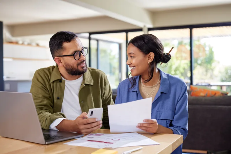 A couple at a table reviewing paperwork and a laptop together