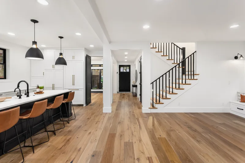 Open main floor with a white kitchen, an island with leather stools, wide oak floors, and a staircase